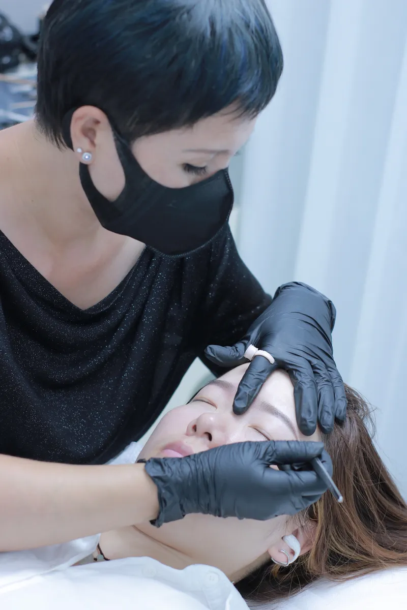 Praticienne professionnelle réalisant une séance de maquillage permanent sur les sourcils d'une cliente